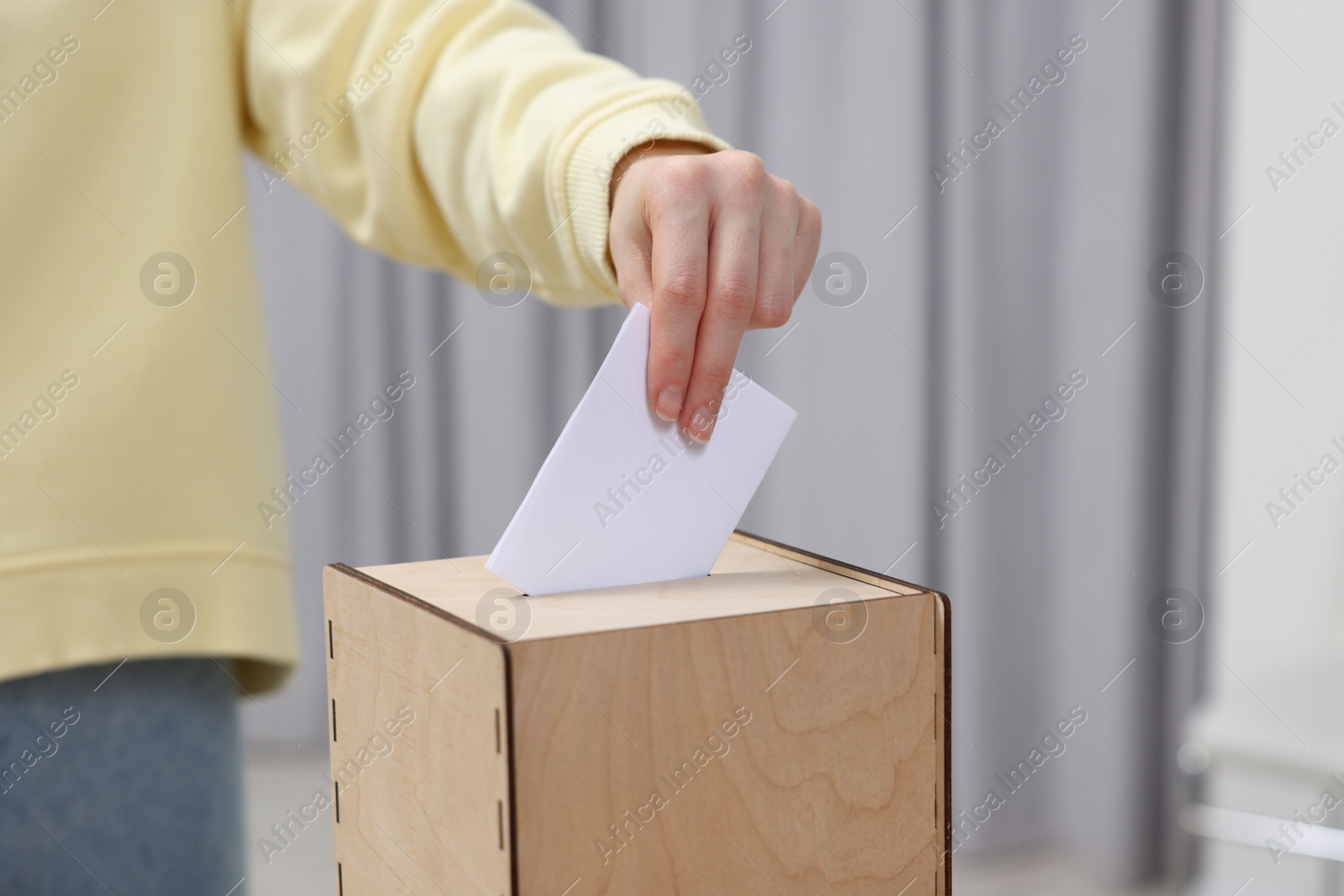 Photo of Woman putting her vote into ballot box on blurred background, closeup