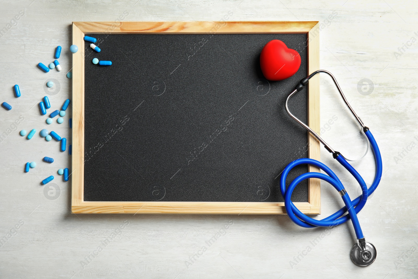 Photo of Stethoscope, pills, heart and blackboard with space for text on light background, top view. Cardiology concept
