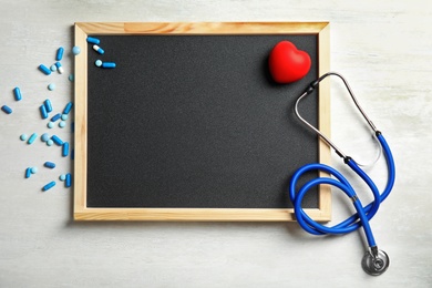 Photo of Stethoscope, pills, heart and blackboard with space for text on light background, top view. Cardiology concept