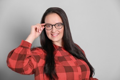 Beautiful overweight woman in eyeglasses on light grey background