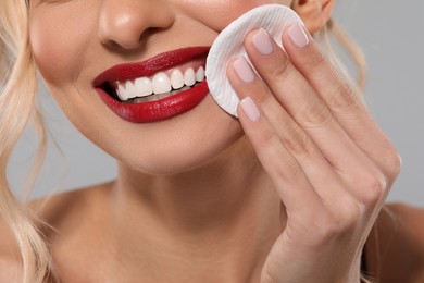 Photo of Smiling woman removing makeup with cotton pad on light grey background, closeup