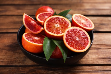 Photo of Whole and cut red oranges with green leaves on wooden table