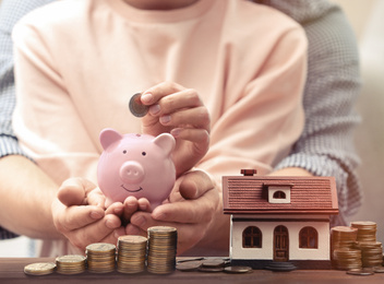 Image of Couple putting money into piggy bank for future house purchase, closeup