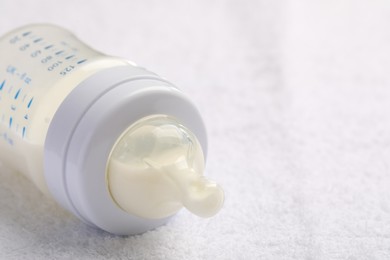 Photo of Feeding bottle with baby formula on white soft towel, closeup. Space for text