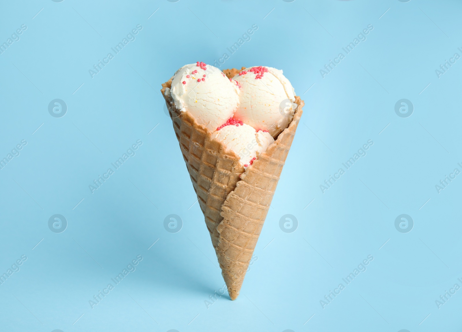 Photo of Delicious vanilla ice cream in wafer cone on blue background