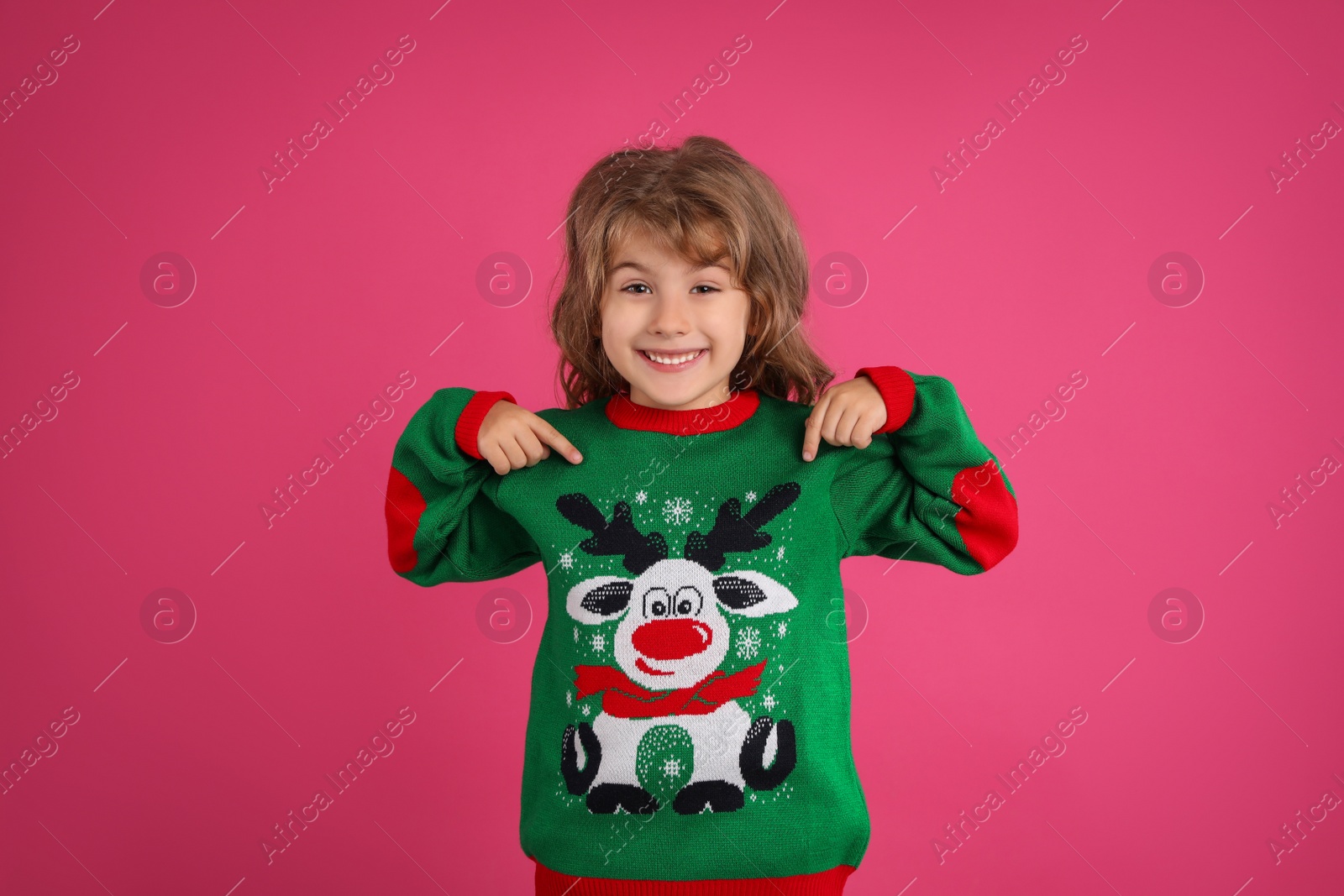 Photo of Cute little girl pointing at her green Christmas sweater against pink background
