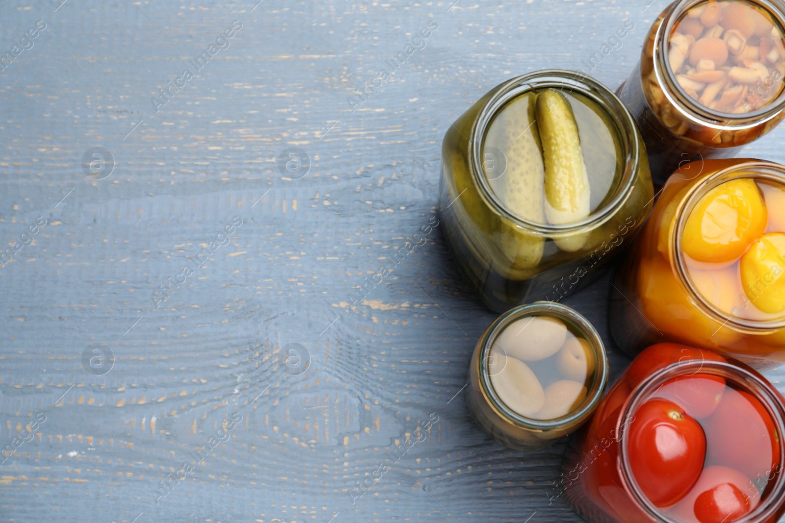 Photo of Glass jars with different pickled vegetables on grey wooden table, flat lay. Space for text