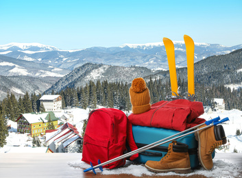 Image of Suitcase with warm clothes on wooden surface against beautiful mountain landscape