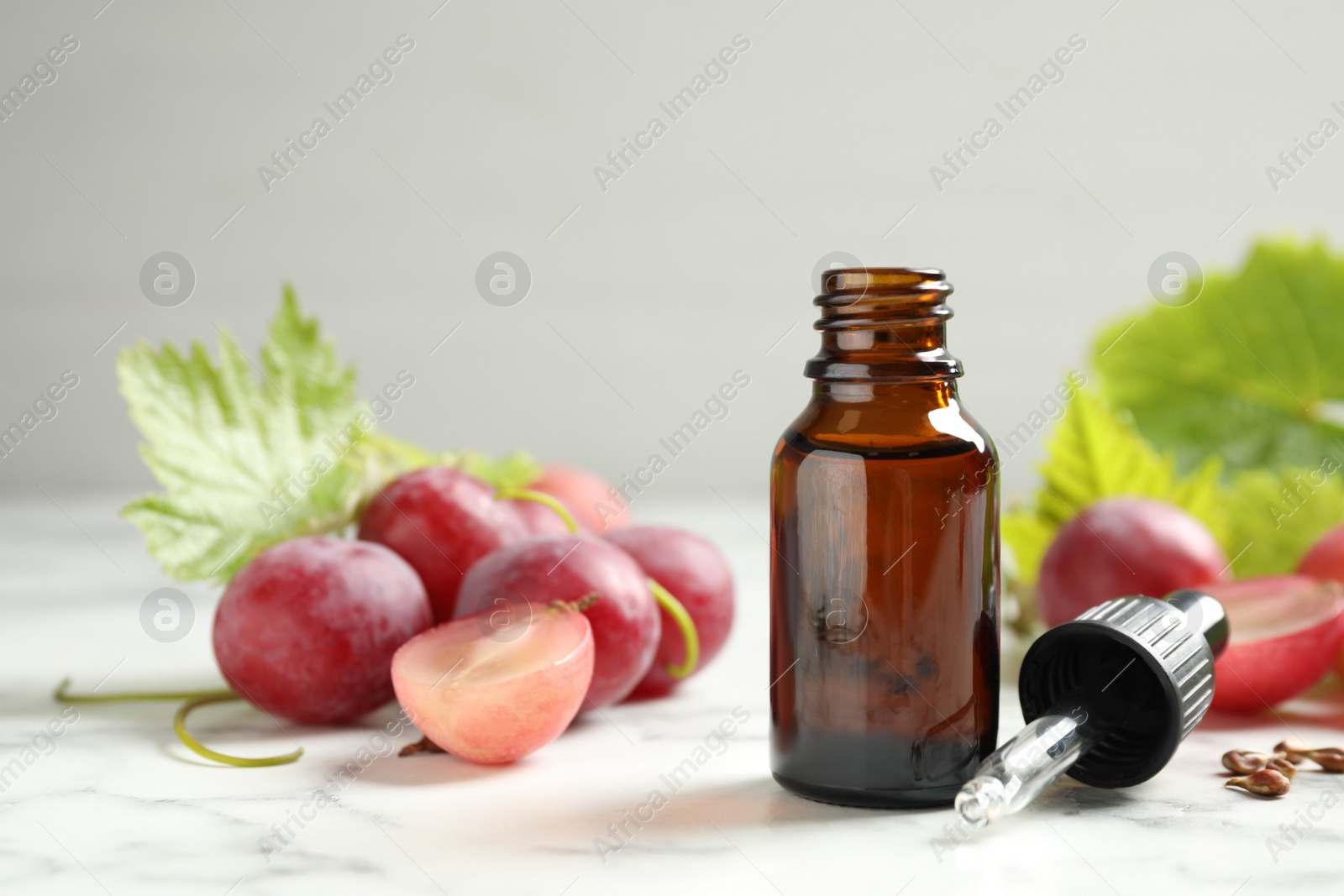 Photo of Bottle of natural grape seed oil on white marble table. Organic cosmetic