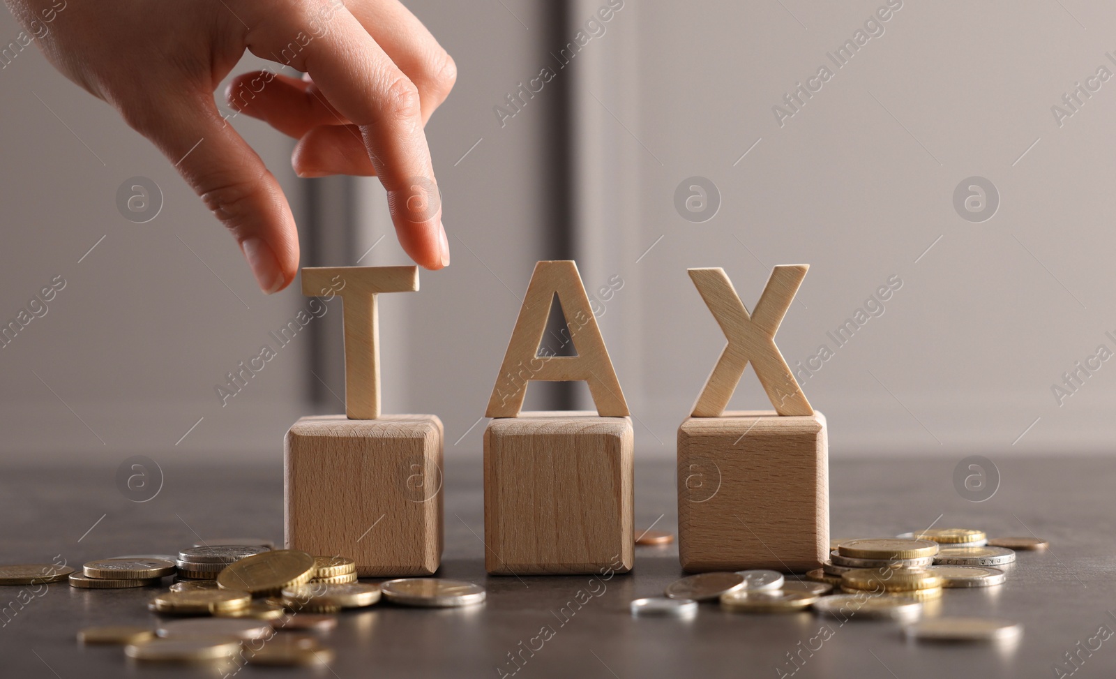 Photo of Woman with word Tax, wooden cubes and coins at grey table, closeup. Space for text