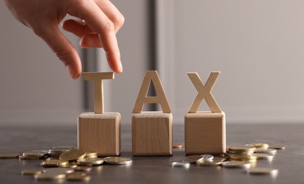 Photo of Woman with word Tax, wooden cubes and coins at grey table, closeup. Space for text