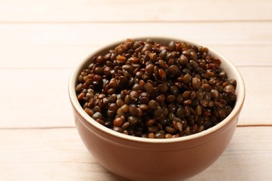 Photo of Delicious lentils in bowl on white wooden table, closeup. Space for text