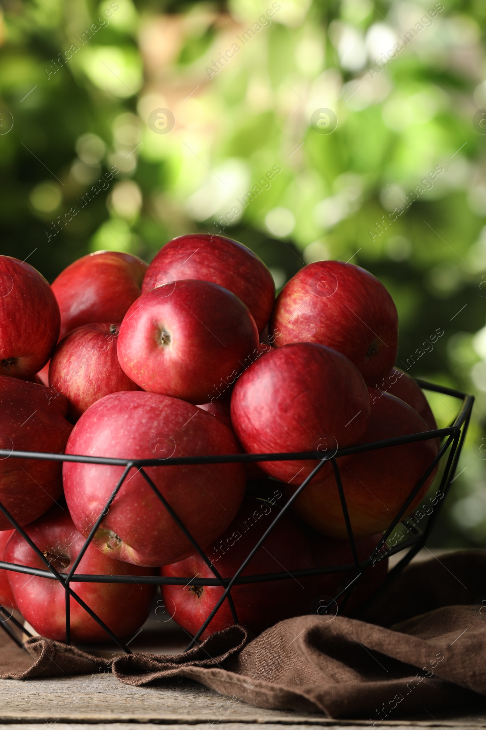 Photo of Ripe red apples in bowl on wooden table outdoors