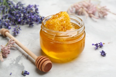Photo of Tasty honey with combs, dipper and lavender flowers on light grey table, closeup