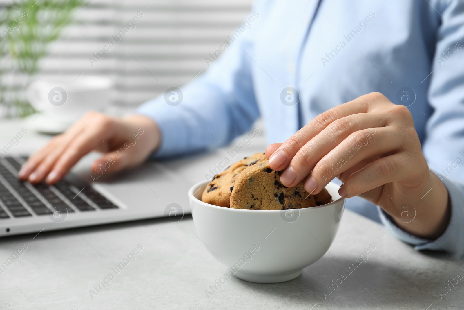 Photo of Office worker taking chocolate chip cookie from bowl at light gray table indoors, closeup