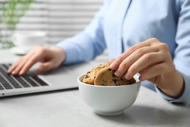 Photo of Office worker taking chocolate chip cookie from bowl at light gray table indoors, closeup