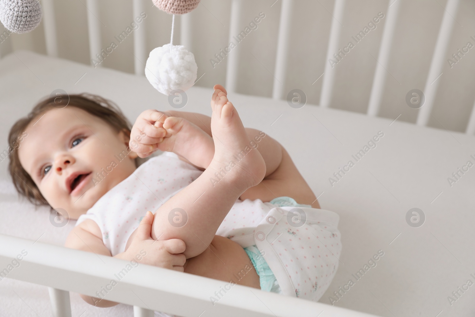 Photo of Cute little baby lying in comfortable crib at home, space for text