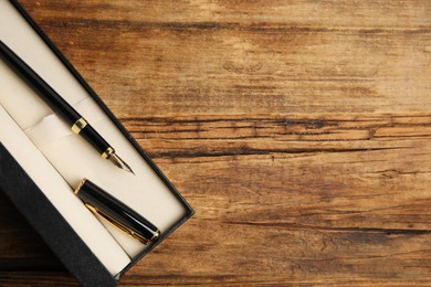 Photo of Beautiful fountain pen in box on wooden table, top view. Space for text