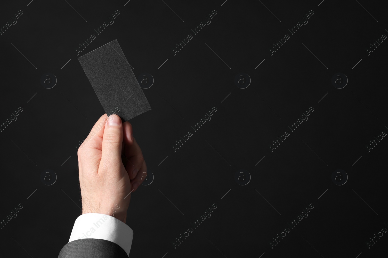 Photo of Businessman holding blank business card on black background, closeup. Space for text