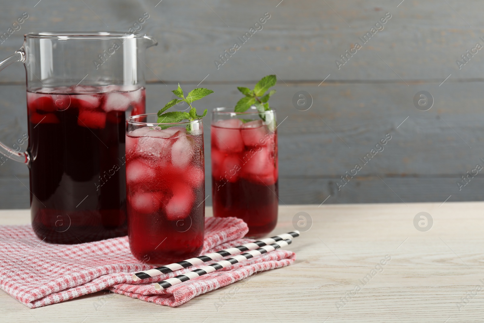 Photo of Delicious iced hibiscus tea with mint and straws on white wooden table, space for text