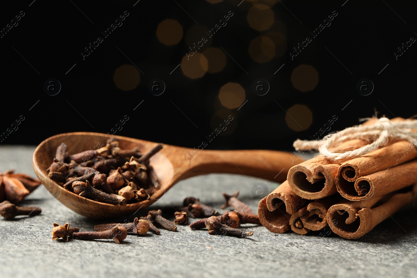 Photo of Wooden spoon with different spices on gray table against black background, closeup