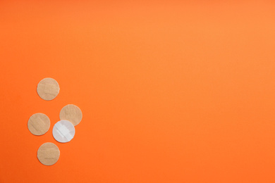 Sticking plasters on orange background, flat lay. Space for text