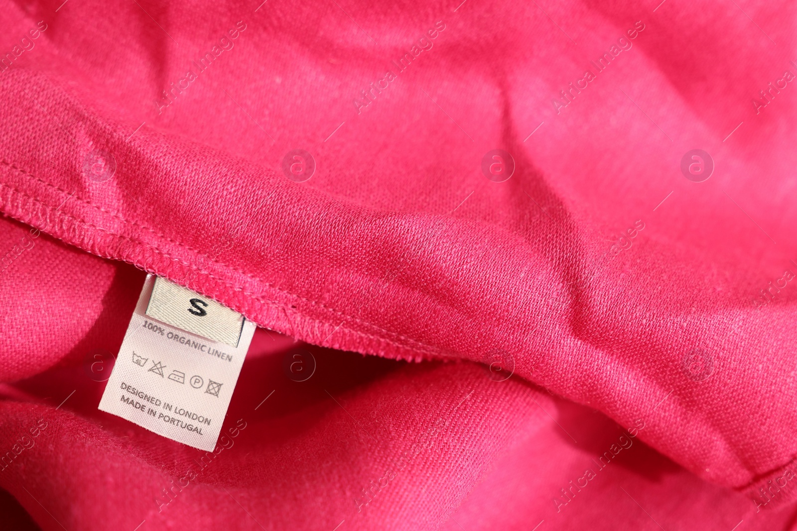 Photo of Clothing label in different languages on pink garment, closeup