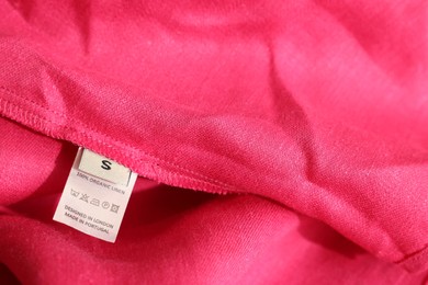 Clothing label in different languages on pink garment, closeup