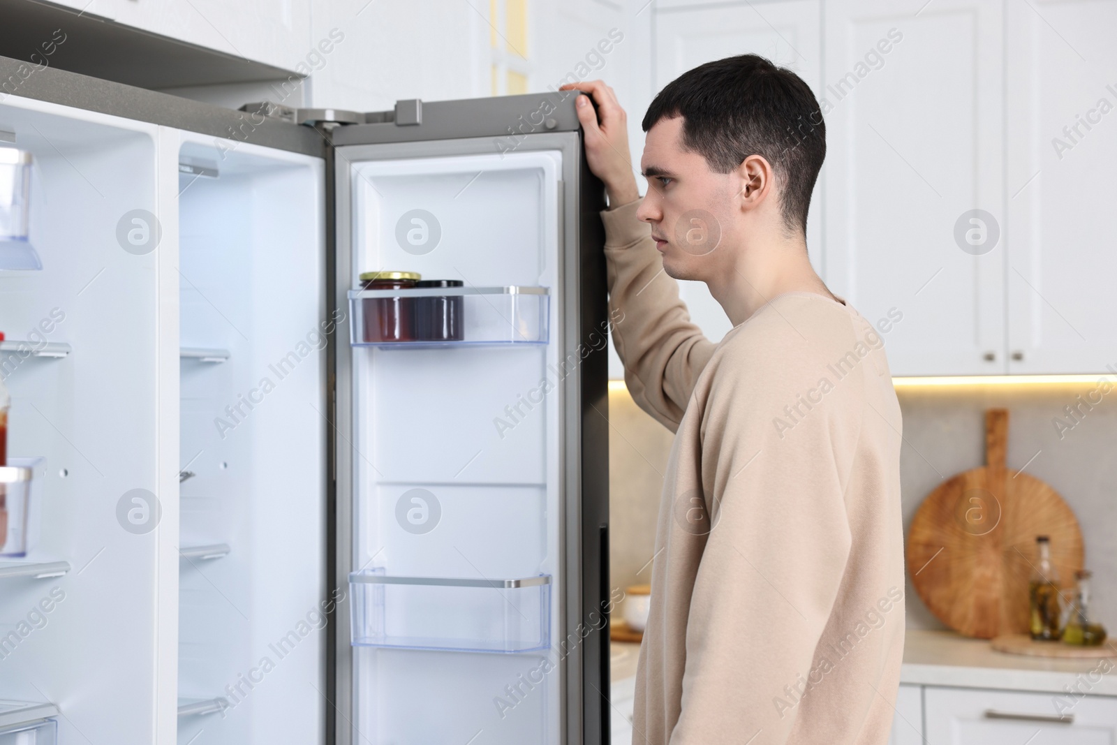 Photo of Upset man near empty refrigerator in kitchen