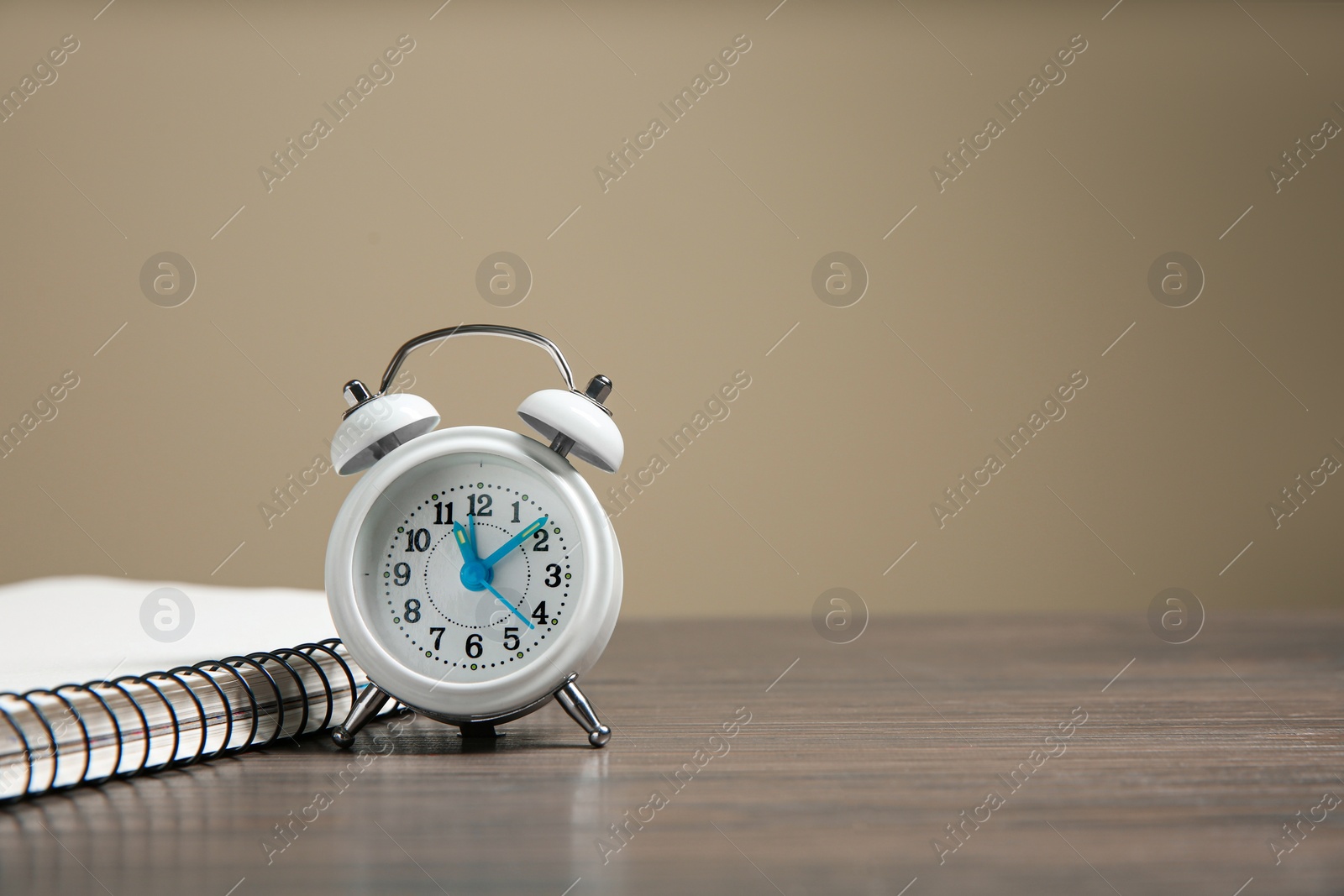 Photo of Alarm clock and notebook on wooden table against beige background, space for text. Time management