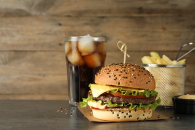 Photo of Burger with delicious patty, soda drink, french fries and sauce on gray table, space for text