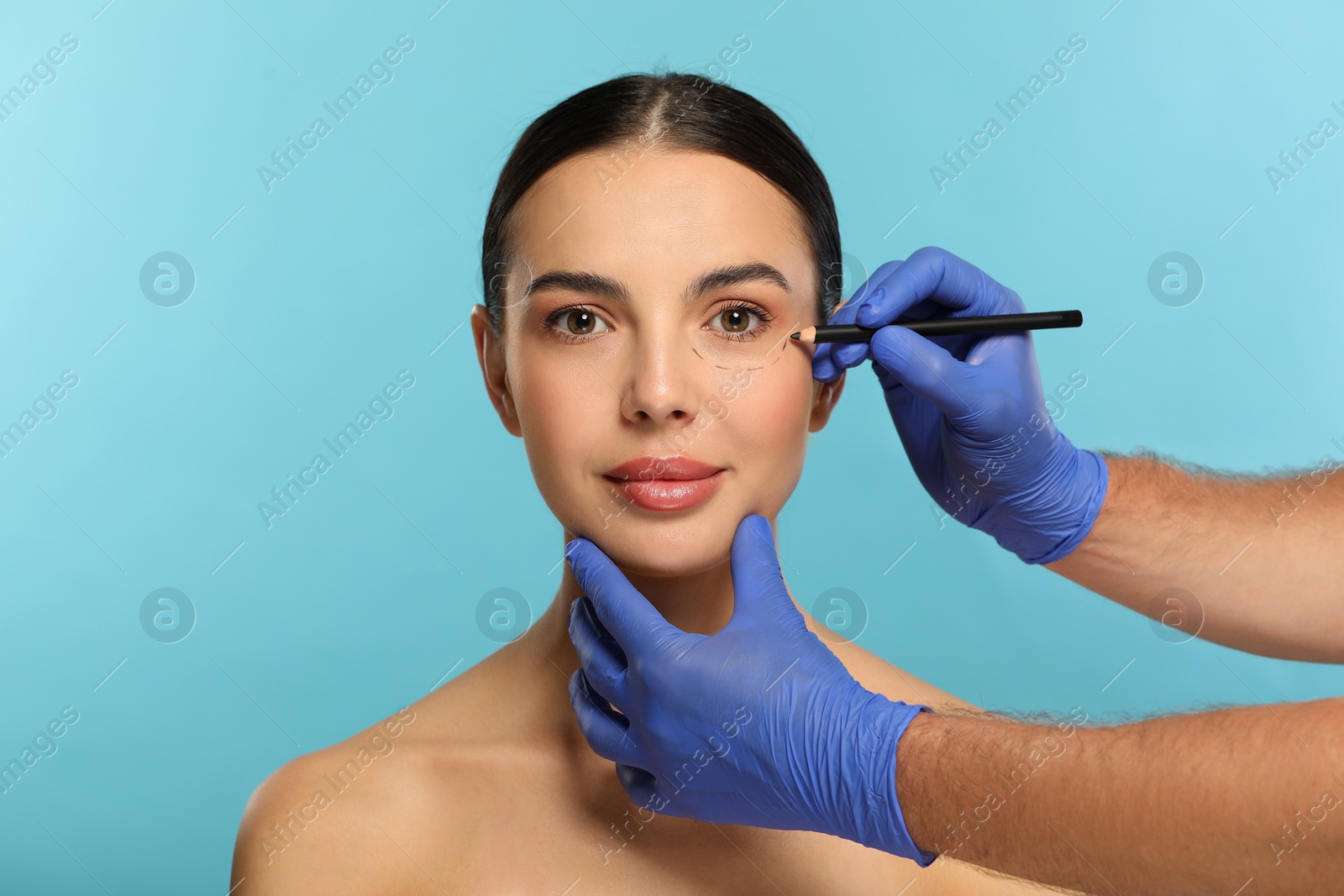 Photo of Doctor with pencil preparing patient for cosmetic surgery operation on light blue background