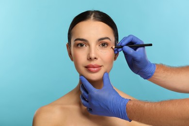 Doctor with pencil preparing patient for cosmetic surgery operation on light blue background