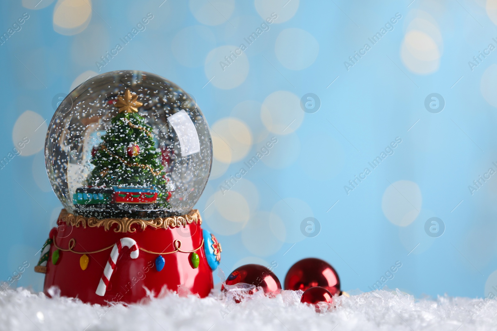 Photo of Beautiful snow globe and baubles against blurred Christmas lights. Space for text