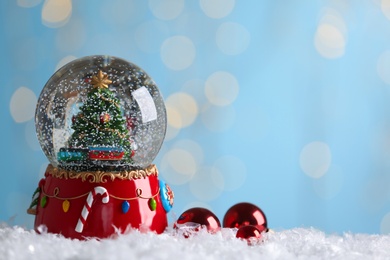 Beautiful snow globe and baubles against blurred Christmas lights. Space for text