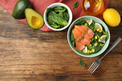 Photo of Delicious salmon with spinach, lemon and avocado served on wooden table, flat lay. Space for text