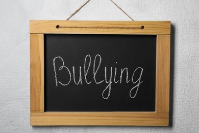 Photo of Blackboard with phrase Bullying on grey wall
