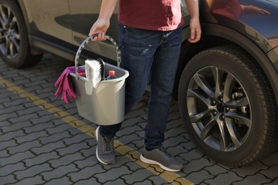 Photo of Man holding bucket with car cleaning products outdoors, closeup