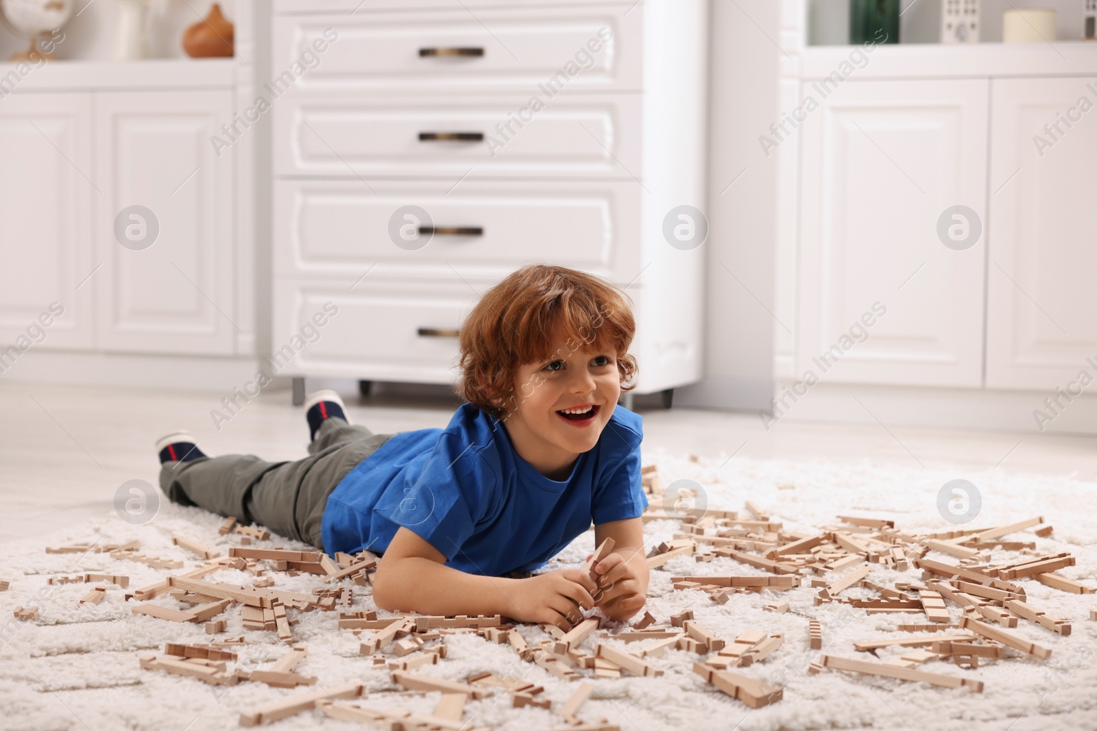 Photo of Cute little boy playing with wooden construction set on carpet at home. Child's toy