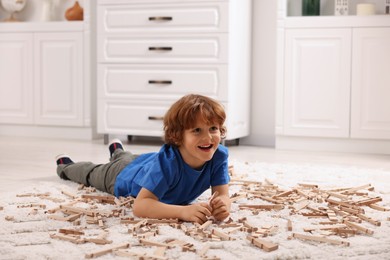 Photo of Cute little boy playing with wooden construction set on carpet at home. Child's toy