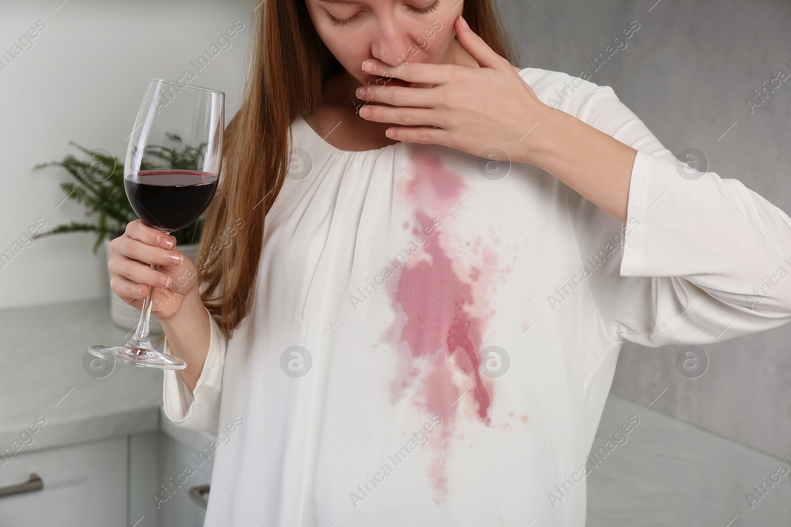 Photo of Embarrassed woman with wine stain on her clothes and glass of wine indoors