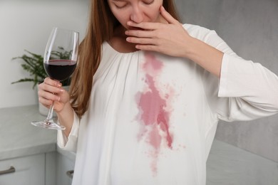 Photo of Embarrassed woman with wine stain on her clothes and glass of wine indoors