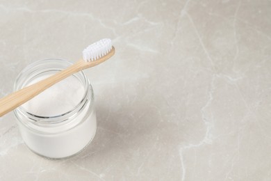 Photo of Bamboo toothbrush and jar of baking soda on light marble table, space for text