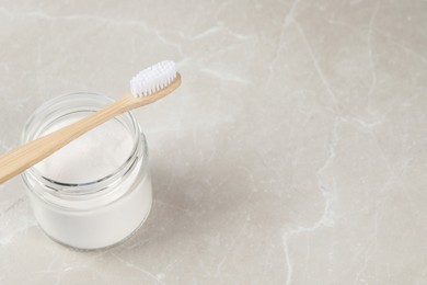 Bamboo toothbrush and jar of baking soda on light marble table, space for text