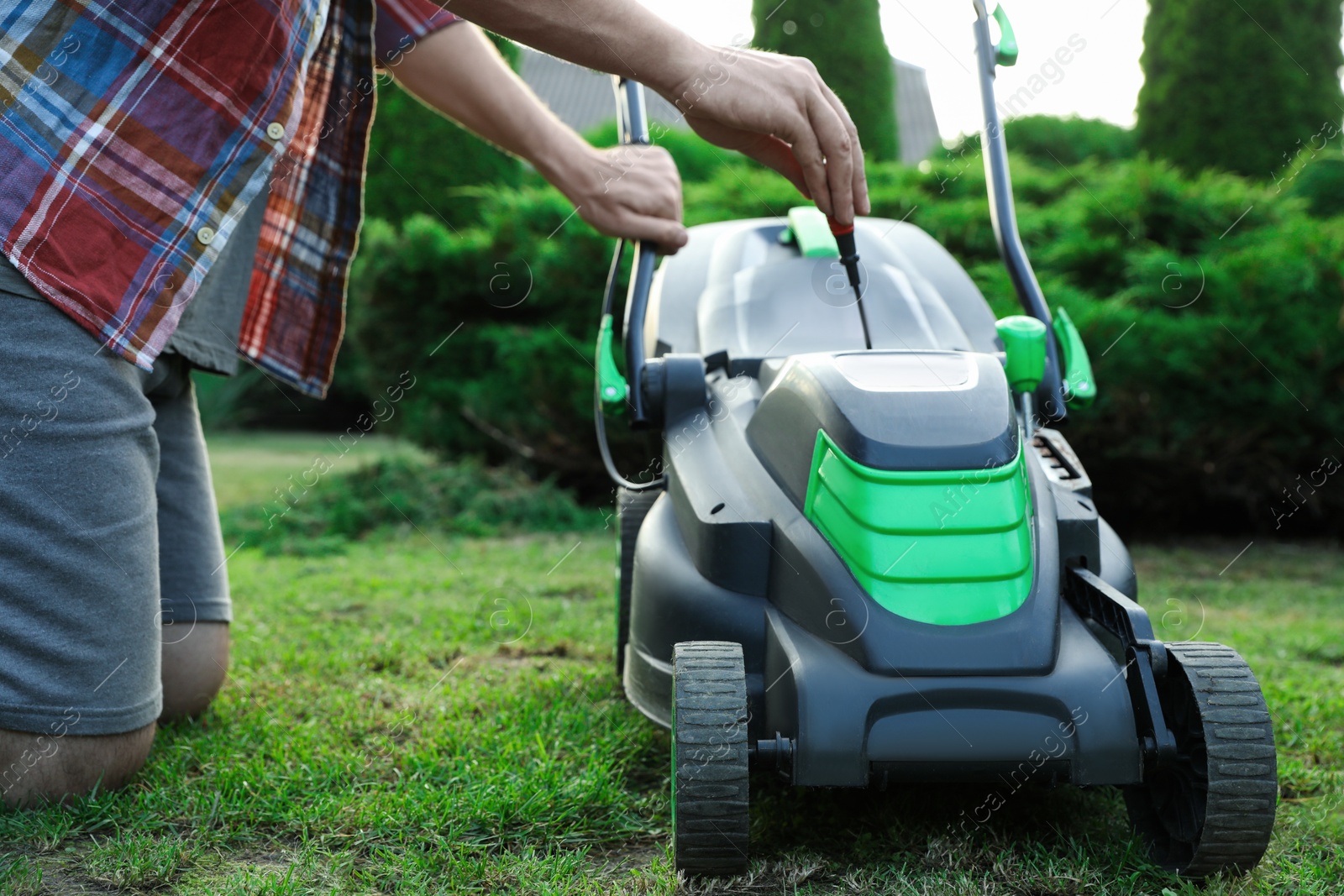 Photo of Man with screwdriver fixing lawn mower in garden, closeup