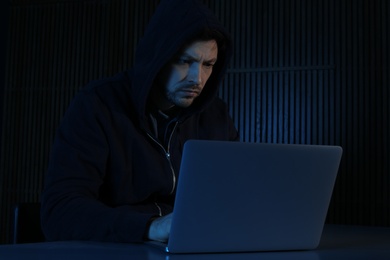 Man using laptop in dark room. Criminal offence