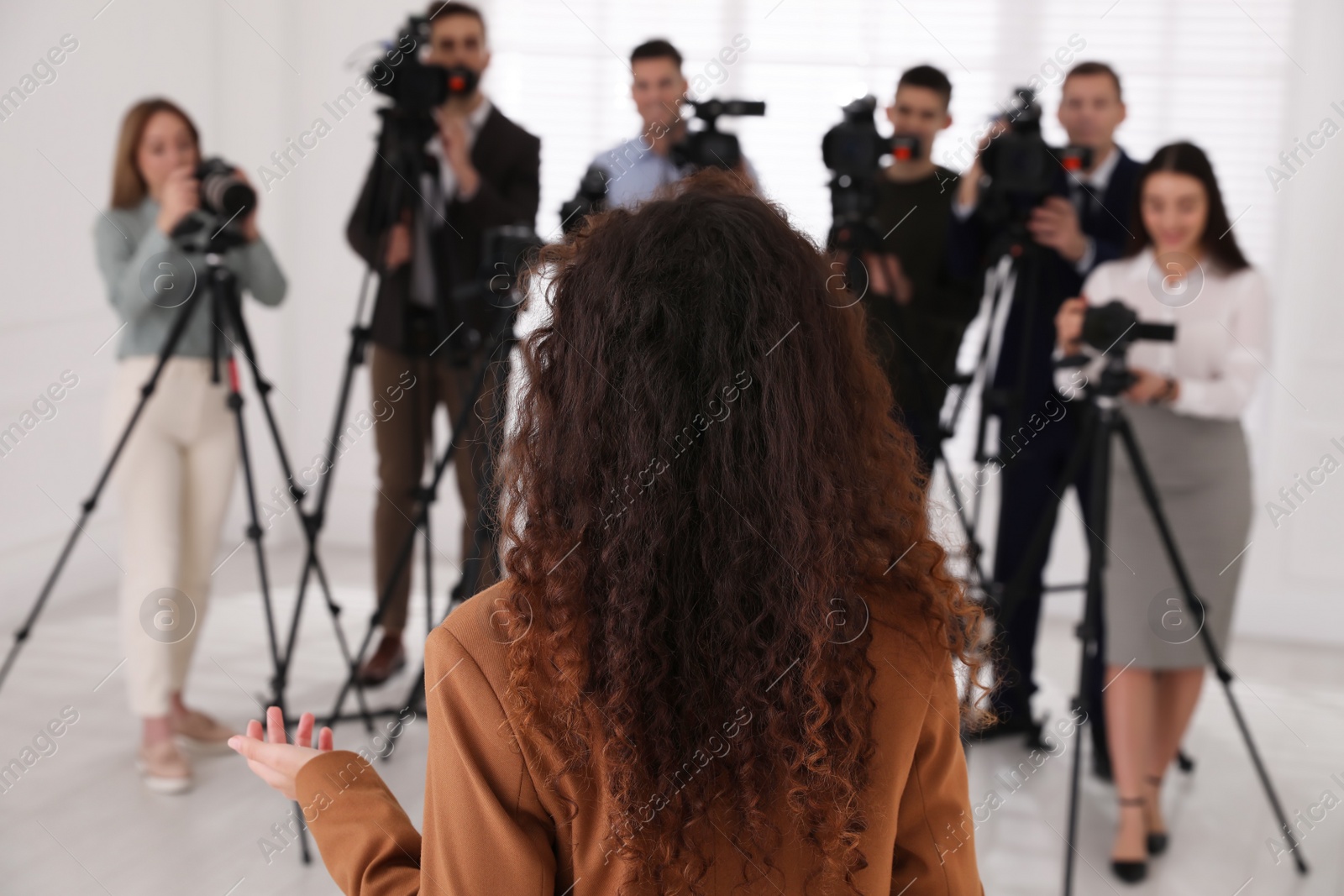 Photo of African American business woman talking to group of journalists indoors, back view