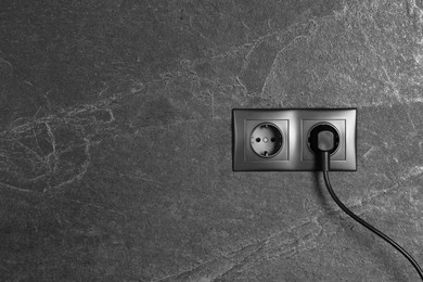 Photo of Power sockets with inserted plug on dark grey wall, space for text. Electrical supply