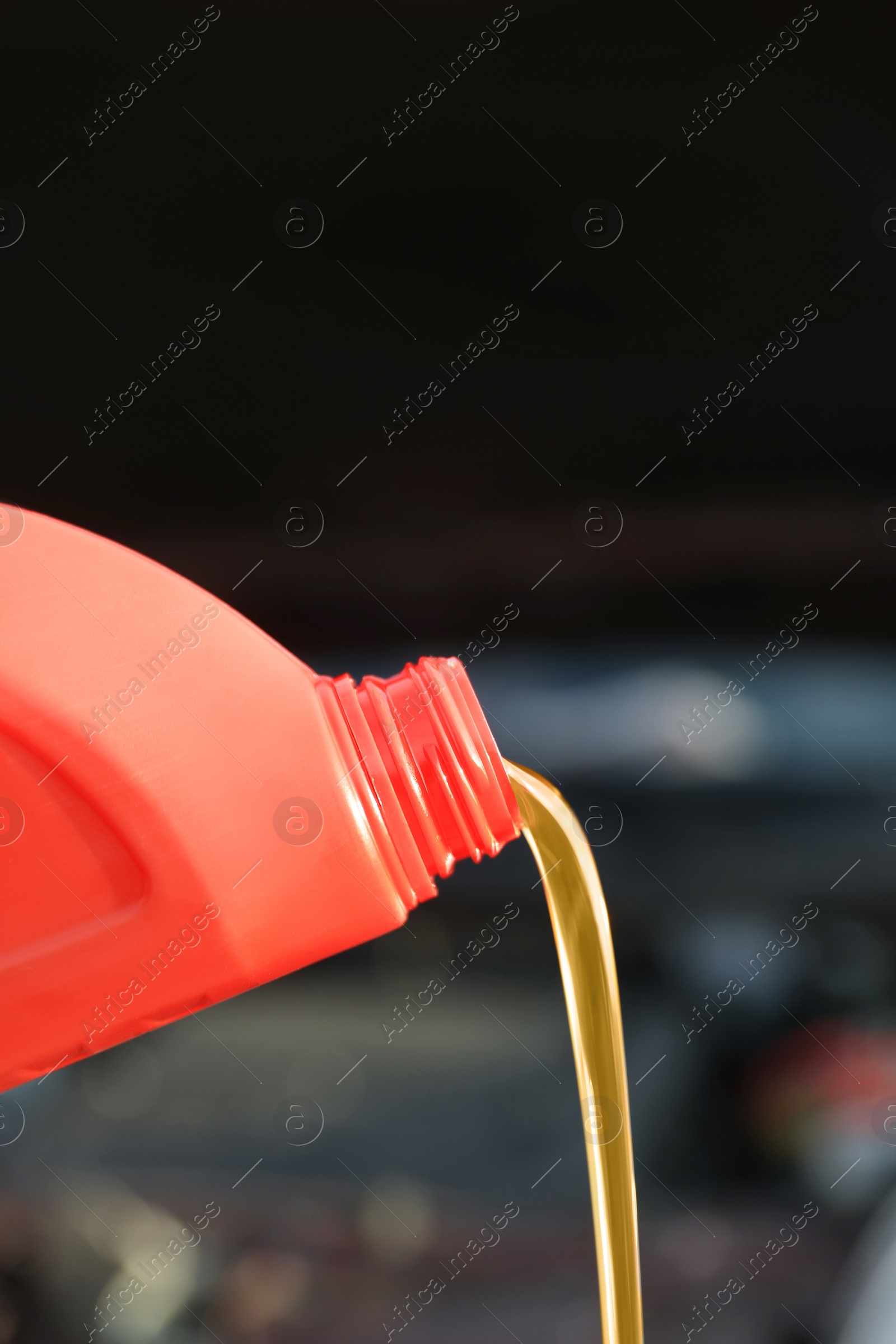 Photo of Pouring motor oil from red container on blurred background, closeup