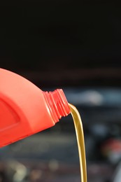 Photo of Pouring motor oil from red container on blurred background, closeup